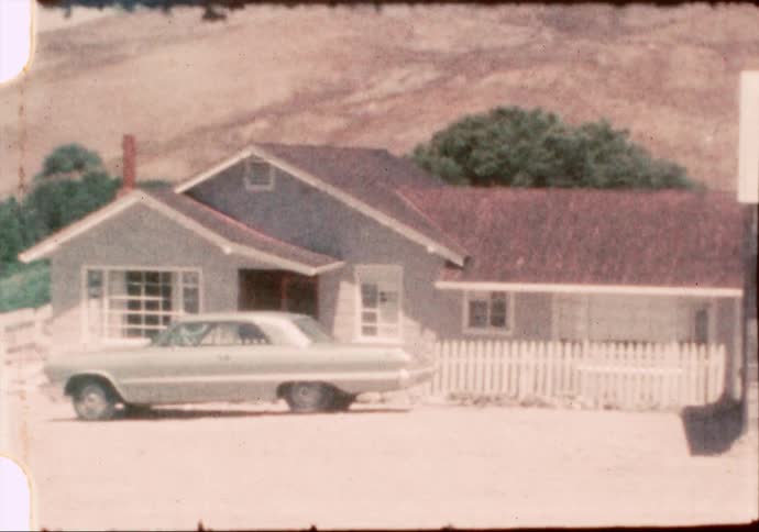 A 1960's Ford sedan sits out front a small mid century home in the rural American west