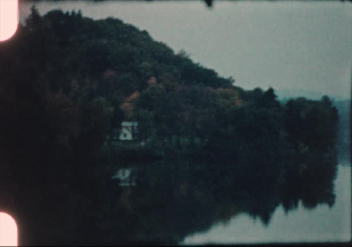 Still river water reflects forest trees on shore on misty day