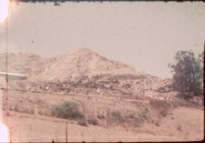 Rocky western hillsides are revealed in a grainy vintage 8mm pan