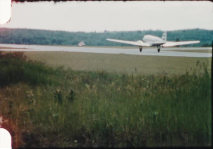 A twin prop commercial airplane takes off down a runway in mid century America