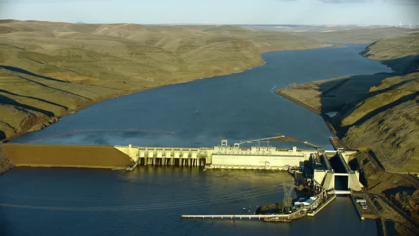 Little Goose Dam with a barge and boat navigation lock on the Lower Snake River as seen from a sweeping aerial shot