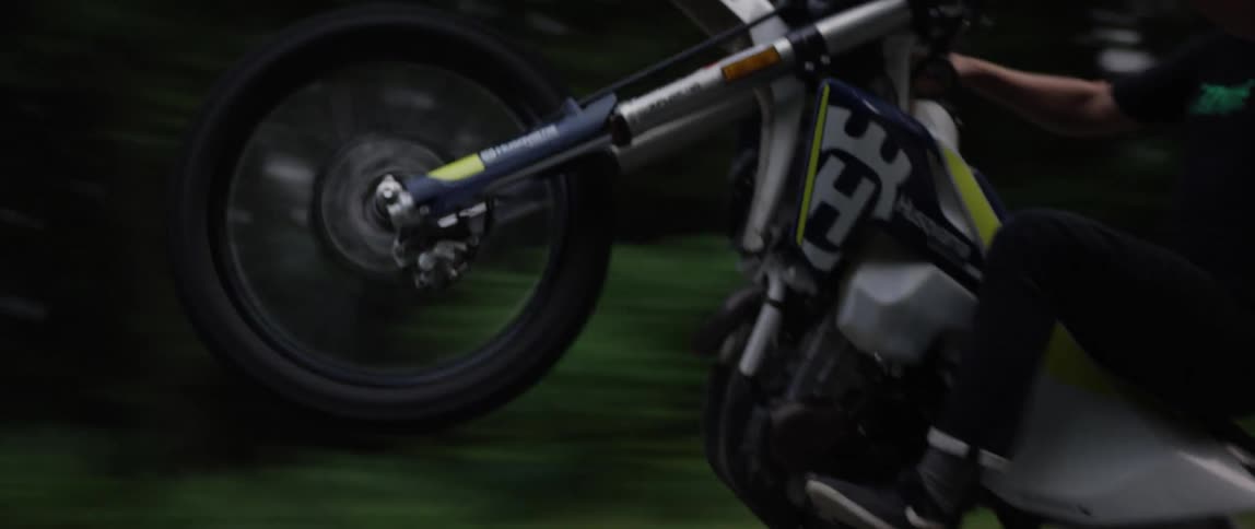 A motorcyclist does a wheelie while speeding down a road through a woodland during the day