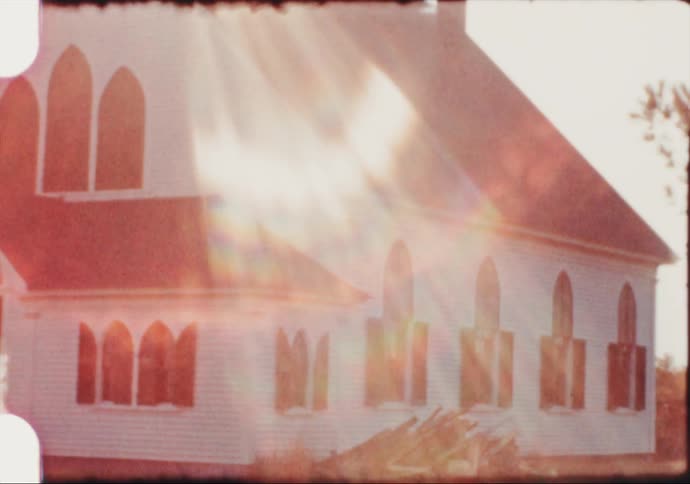 The sun flares across a country church painted white