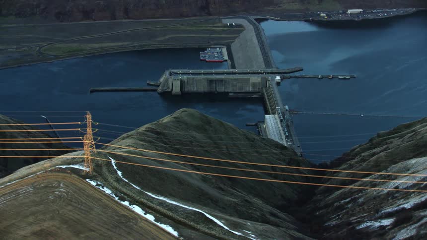 Dynamic aerial featuring high tension power lines looking straight down valley at Lower Granite Dam on the Lower Snake River as the camera wraps around the dam
