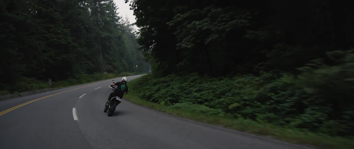 A person with a helmet riding on a motorcycle on a road surrounded by trees with the sky and clouds in the background