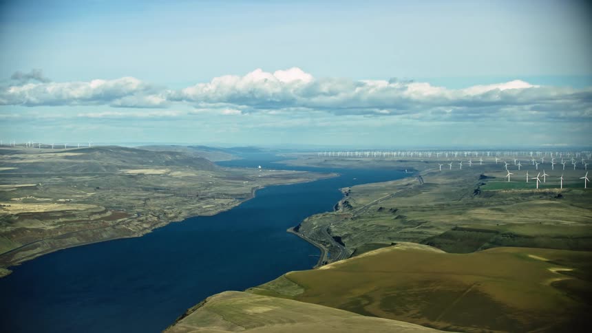 The eastern Columbia River Gorge high above the Deschutes River with vast wind farms producing renewable energy and hydro power under a puffy cloud blue sky day