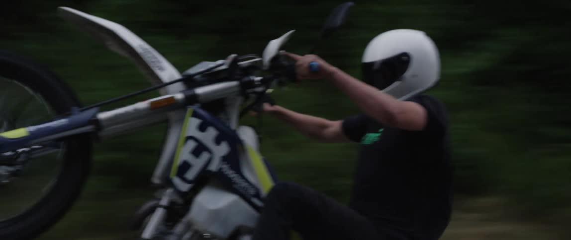 A motorcyclist does a wheelie while riding on a curved road in the countryside
