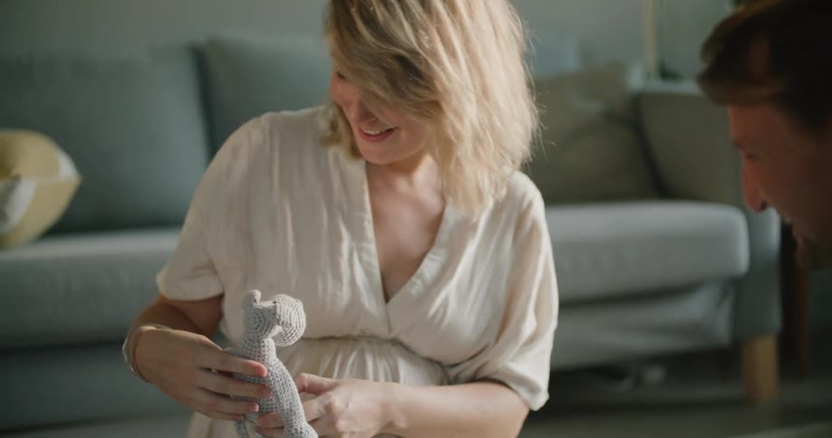 A pregnant woman smiling while looking at baby toys on a living room floor