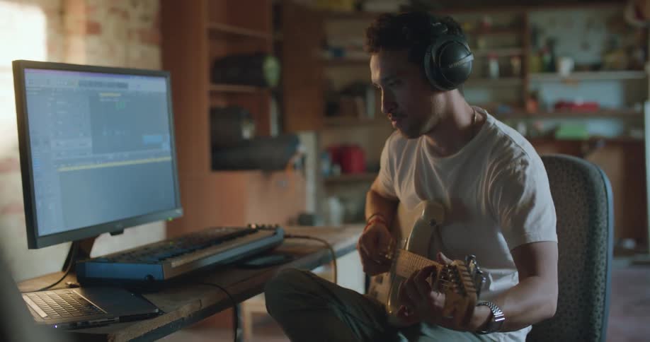 A man plugs his guitar into his computer to record and starts playing