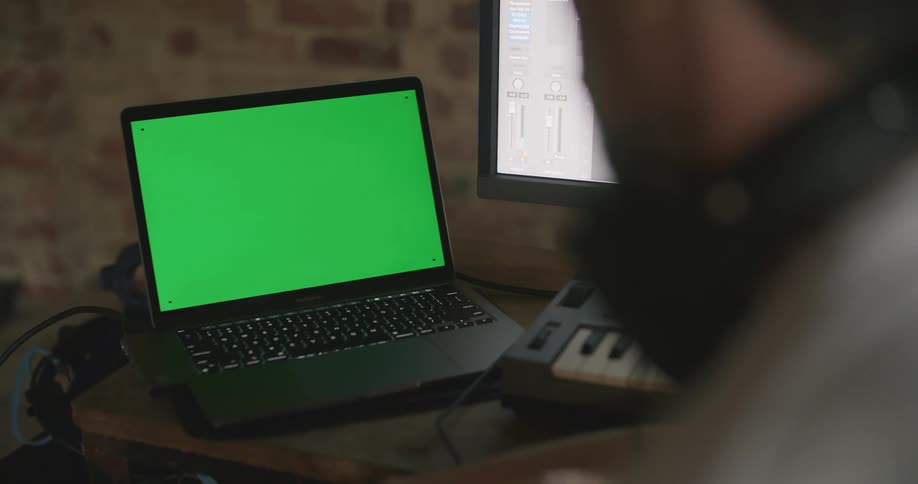 A person with headphones sitting at a desk with a laptop keyboard and a computer
