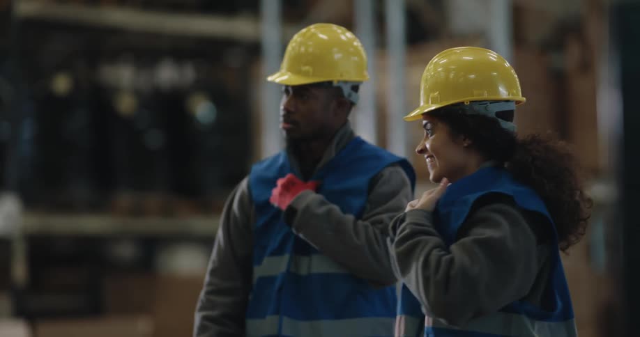 Two men and a woman with hardhats in a warehouse with shelves in the background
