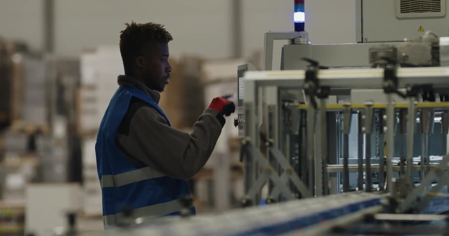 A man with a vest and gloves in a warehouse with a woman in the background