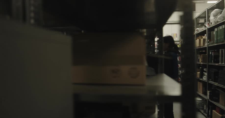 A man with a vest and a basket walking in a warehouse with shelves