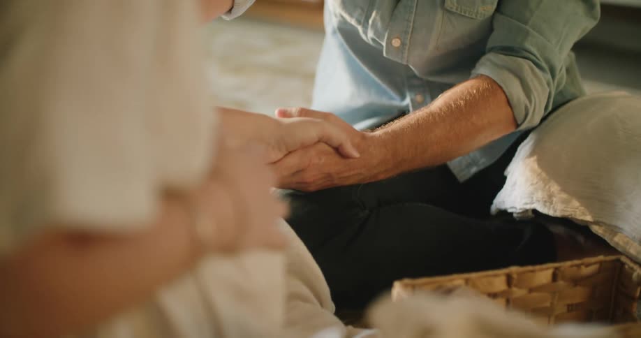 Young pregnant couple talking while holding hands sitting in the livingroom at home