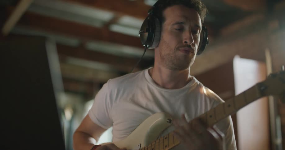 A man is playing guitar and wearing headphones