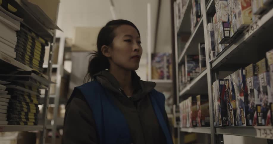 A woman walks down an aisle in a warehouse to check boxes on shelves