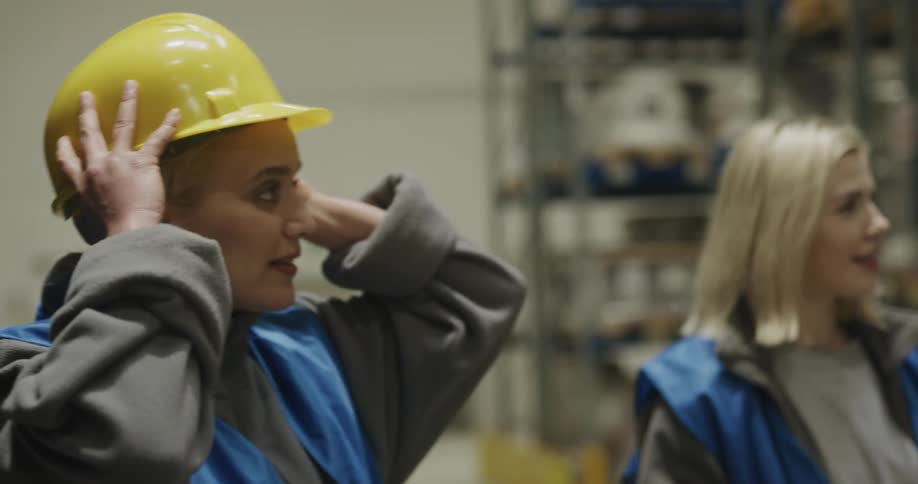 Two women with hardhats and vests walking in a warehouse with shelves in the background