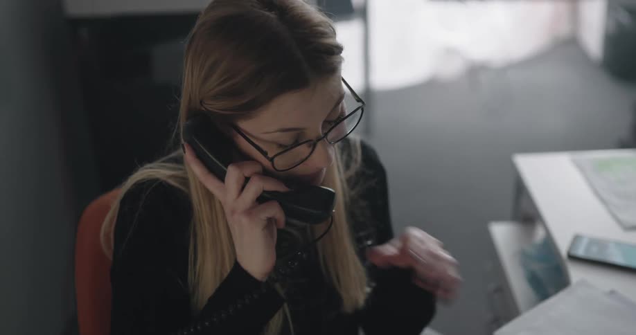 A woman speaks on an office phone while sitting at a desk during the day