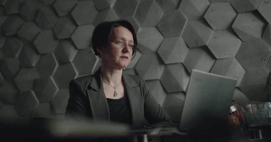 A woman using a laptop in a office stops for a moment to speak with someone out of frame