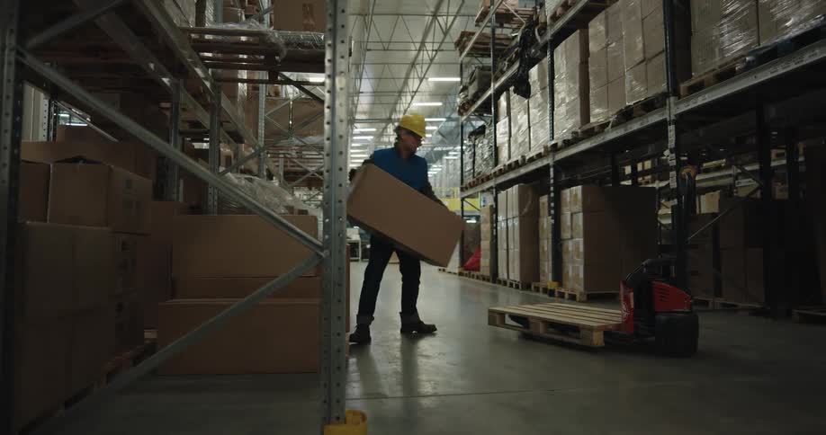 A man with a hardhat placing a box onto a forklift in a warehouse