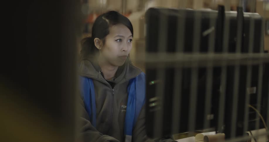 A woman working in a warehouse types on a computer keyboard and looks at the screen