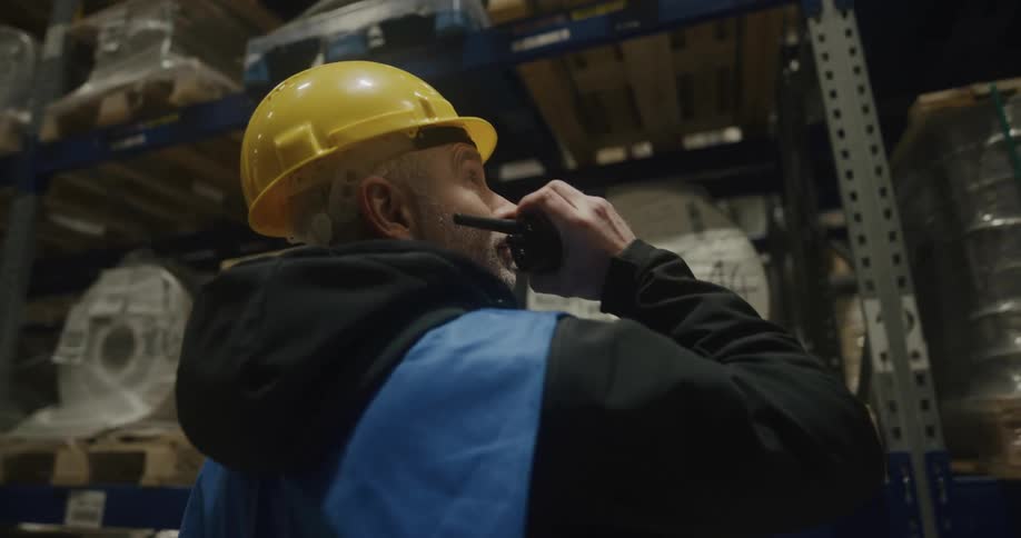 A warehouse worker in a hard hat talking into a walkie talkie