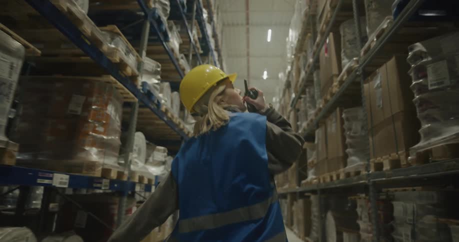 A woman walking around a warehouse talking on a walkie talkie
