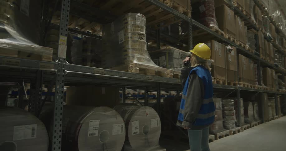 Warehouse worker checking pallets of products in the aisles while talking on a walkie talkie