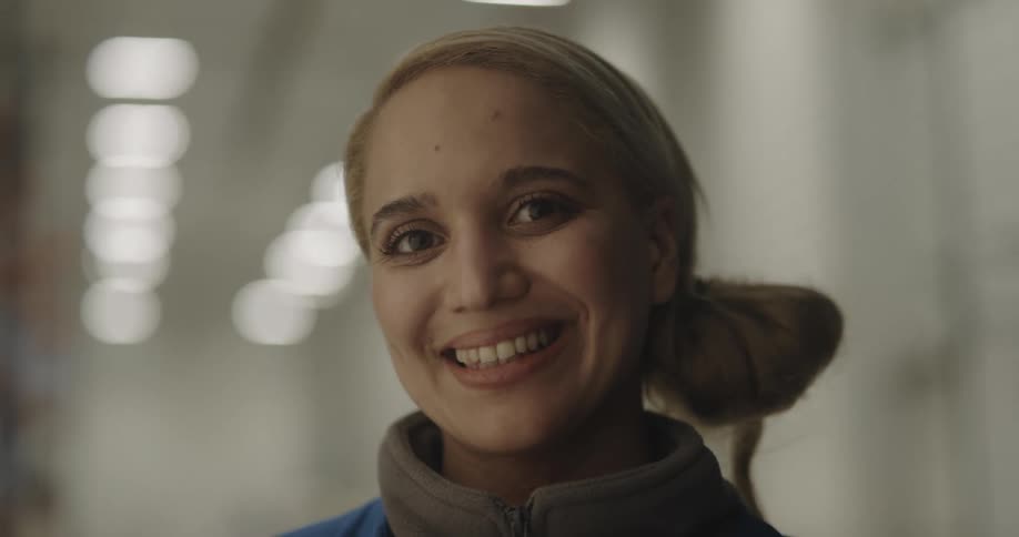 A woman with a vest standing and smiling in a warehouse with lights in the background