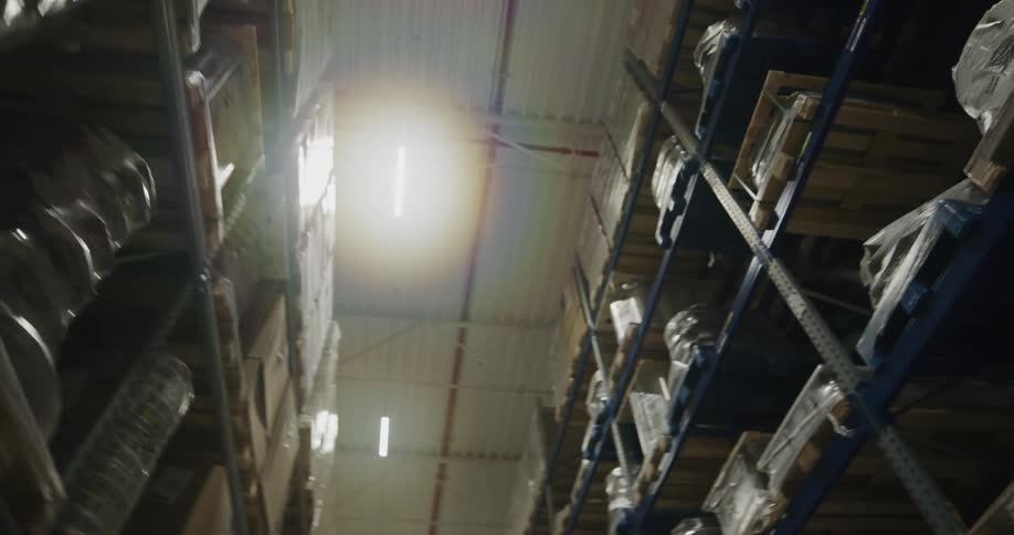 A warehouse with shelves boxes and pallets with lights above