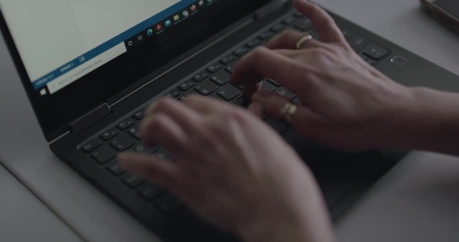 A person typing on the keyboard of a black laptop over a desk