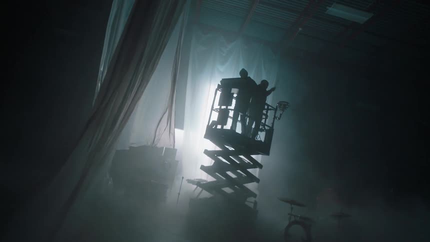 Two musicians play drums and keyboard as they are raised on a platform on a stage
