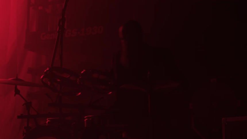 Band plays on pink tinted stage as cherry picker platform rises in background