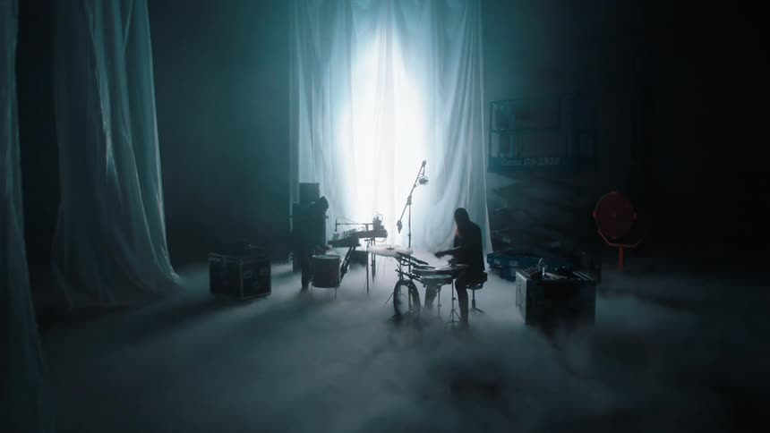 Two musicians play drums on a set designed for filming