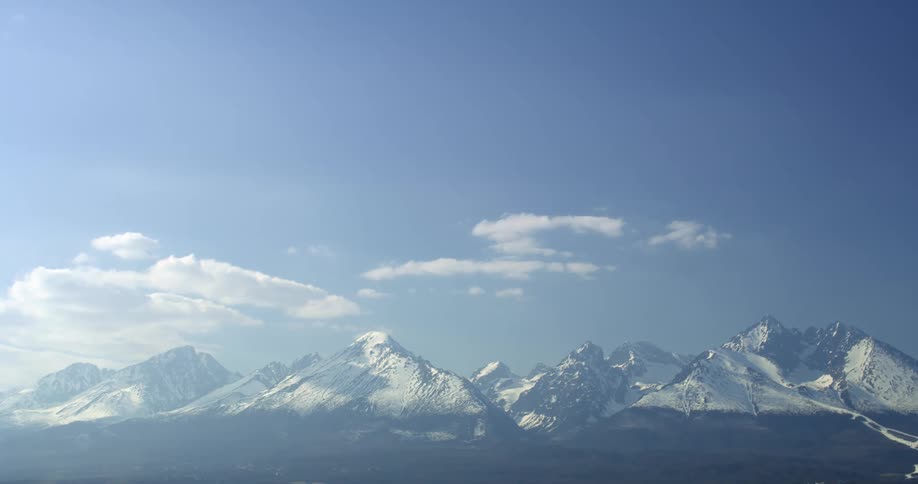 Light clouds hover over snow capped mountain peaks