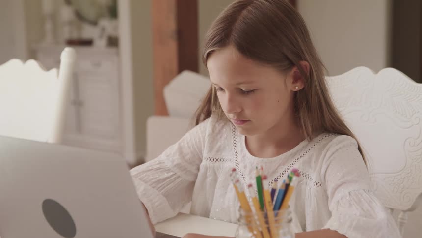 Young girl doing homework on a laptop in a room at home