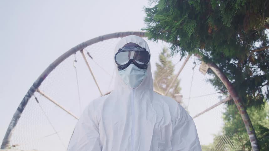 A person with a hazmat suit and goggles with trees the sky and clouds in the background
