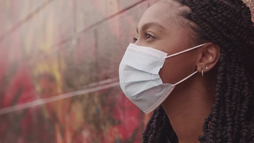 Woman with braids earrings and a white mask looks up