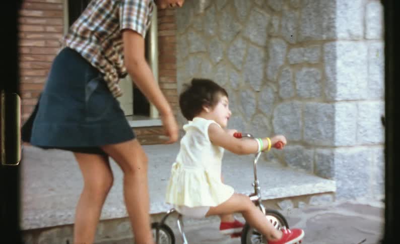 A child is riding a tricycle with some help