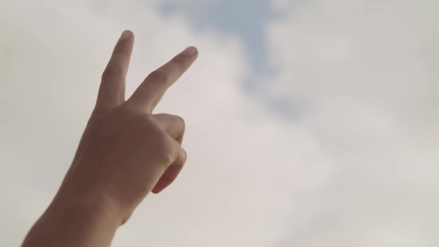 A persons hand in the air with two fingers up with the sky and clouds in the background