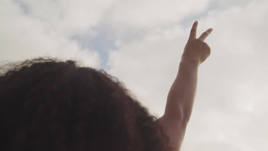 A woman with her hand in the air with two fingers up to the sky with clouds up above