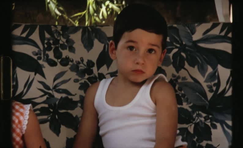 A boy and a girl sitting on a chair with a wall in the background