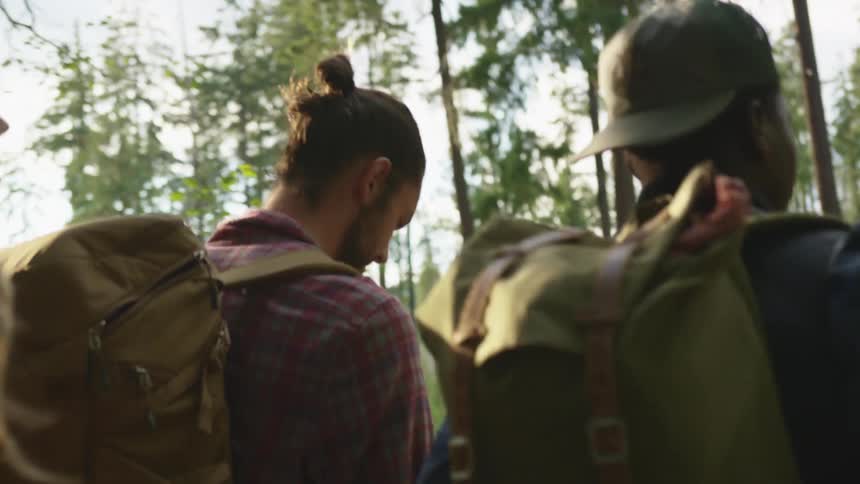 Group of friends carrying backpacks walking in the forest at sunset