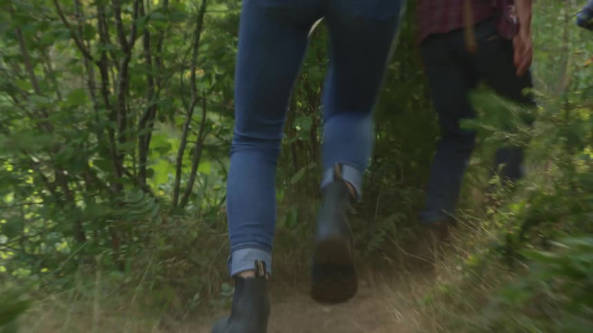 People with jeans and boots running on a dirt pathway surrounded by plants