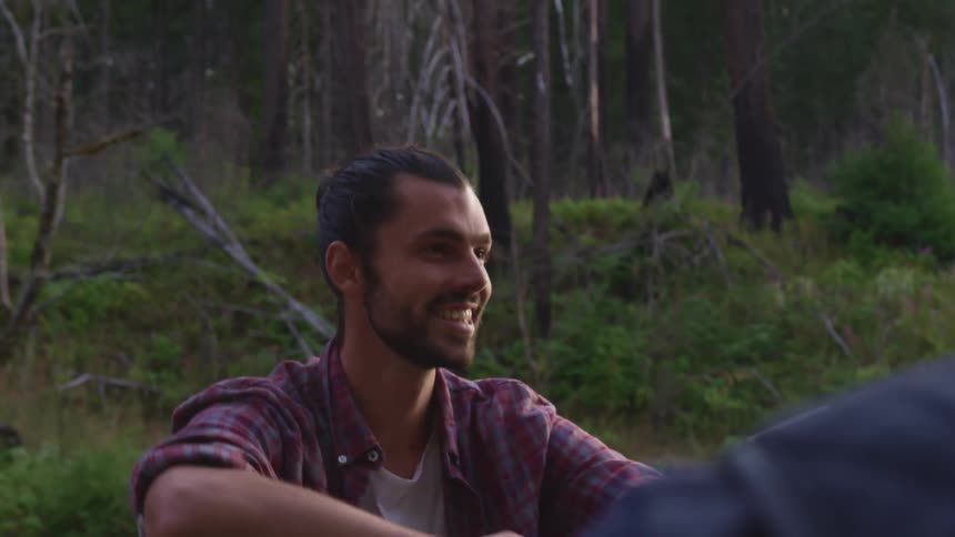 A man sitting and talking with a forest plants and trees in the background