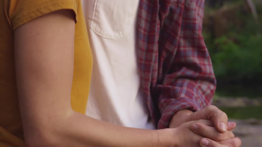 A man and woman hold hands and slow dance in a forest