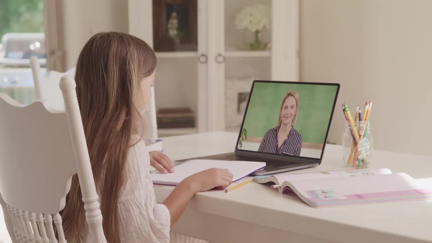 Girl studying at home waving at the teacher in an online class through a laptop