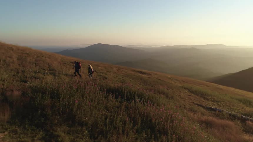 Couple carrying backpacks climbing the slope of a mountain at sunset