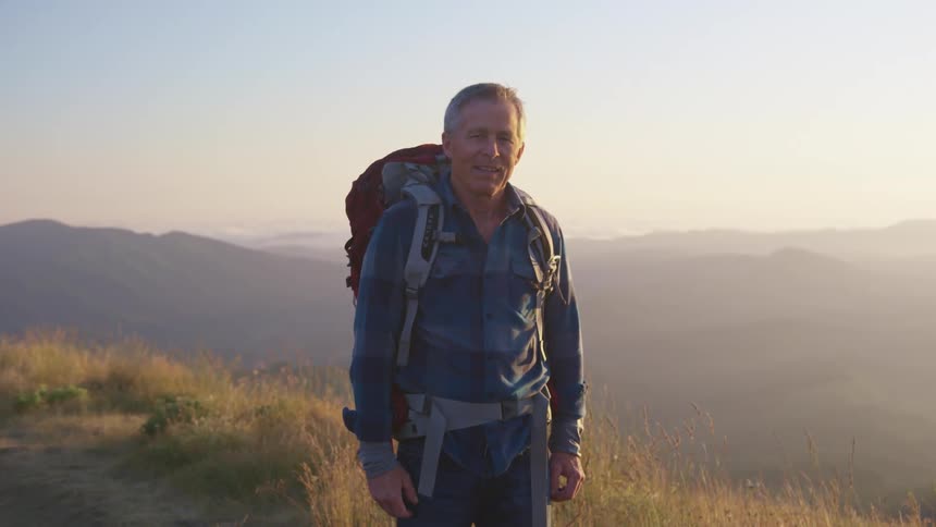 A man wearing a large backpack stands on a hill smiling