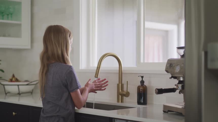 Young long haired blonde woman washes her hands with liquid soap in the kitchen sink